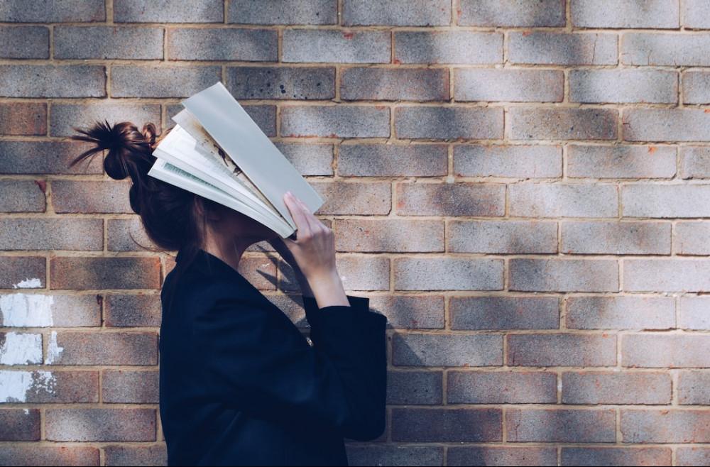 Woman with folders over her face standing next to a brick wall